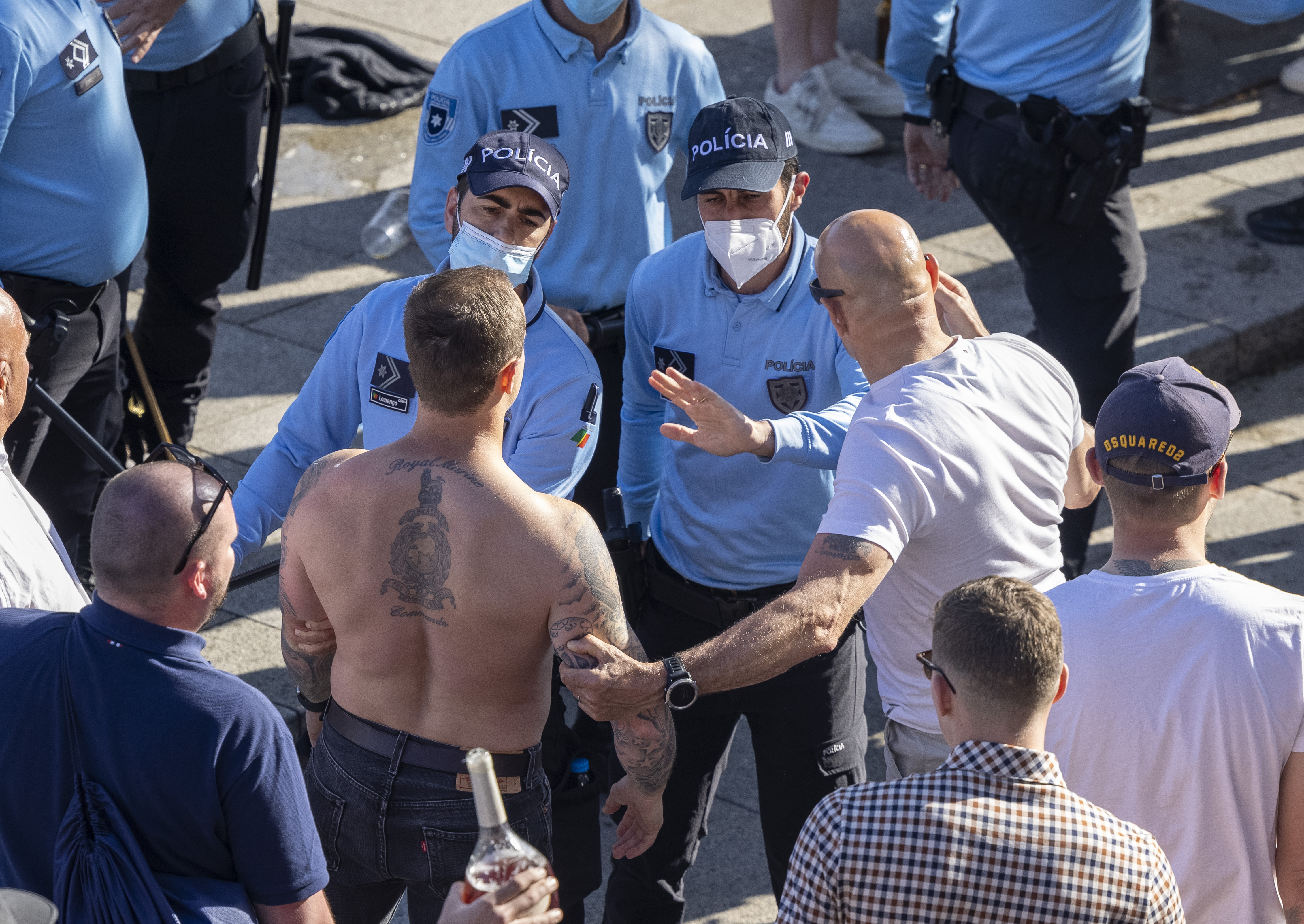 A shirtless man covered in tattoos speaks to police officers
